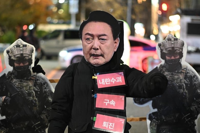 A protester wears a mask showing the face of South Korean President Yoon Suk Yeol.