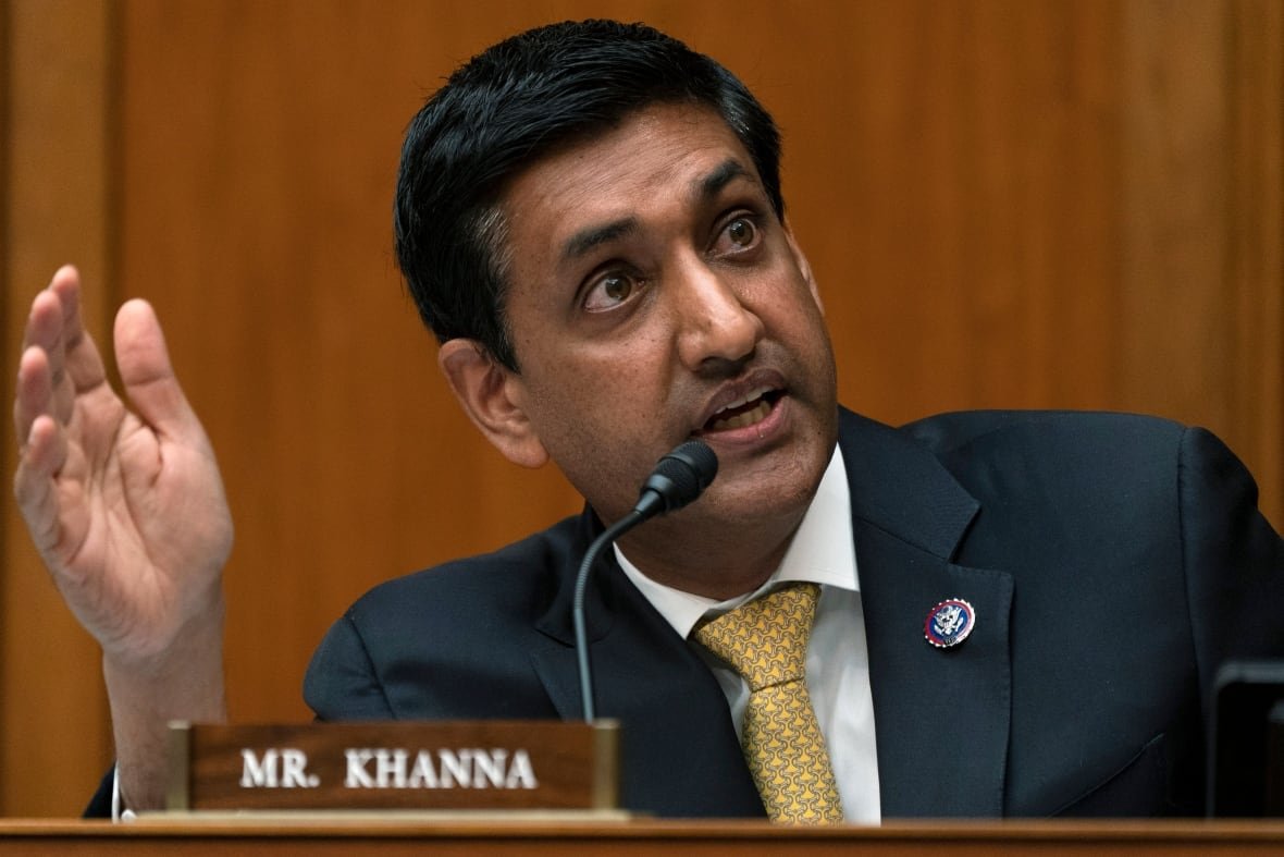 A man in a suit speaks into a microphone and gestures. 