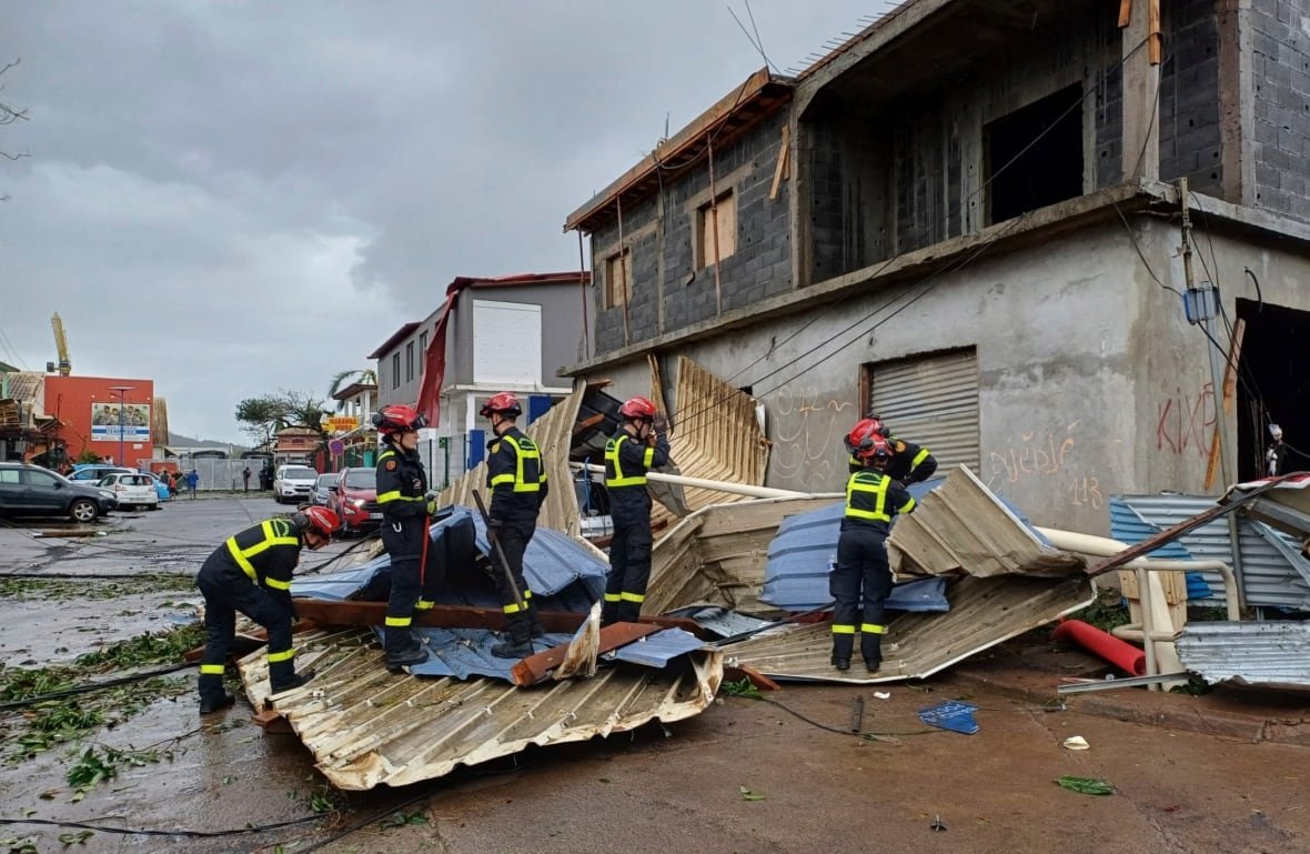 Rescue workers clear debris on a road next to a heavily damaged building.