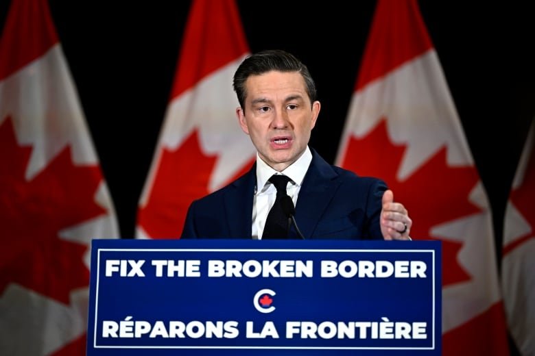 A person gestures while speaking at a lectern adorned with a sign that reads, 'Fix the broken border.'