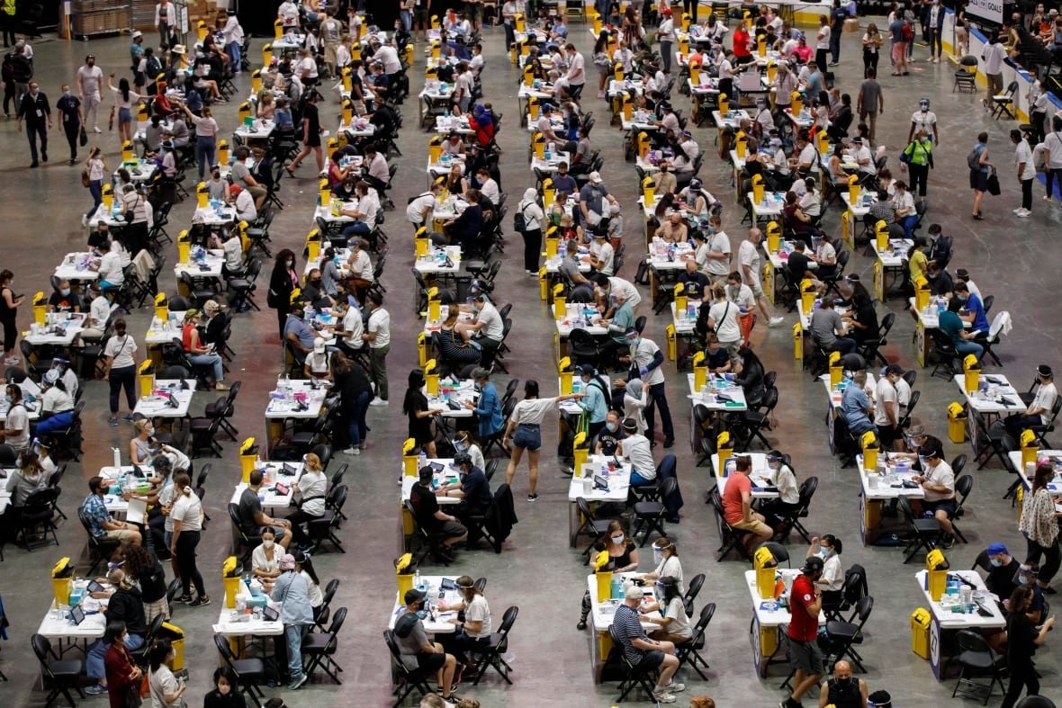 People sit at tables in an arena waiting to be vaccinated.