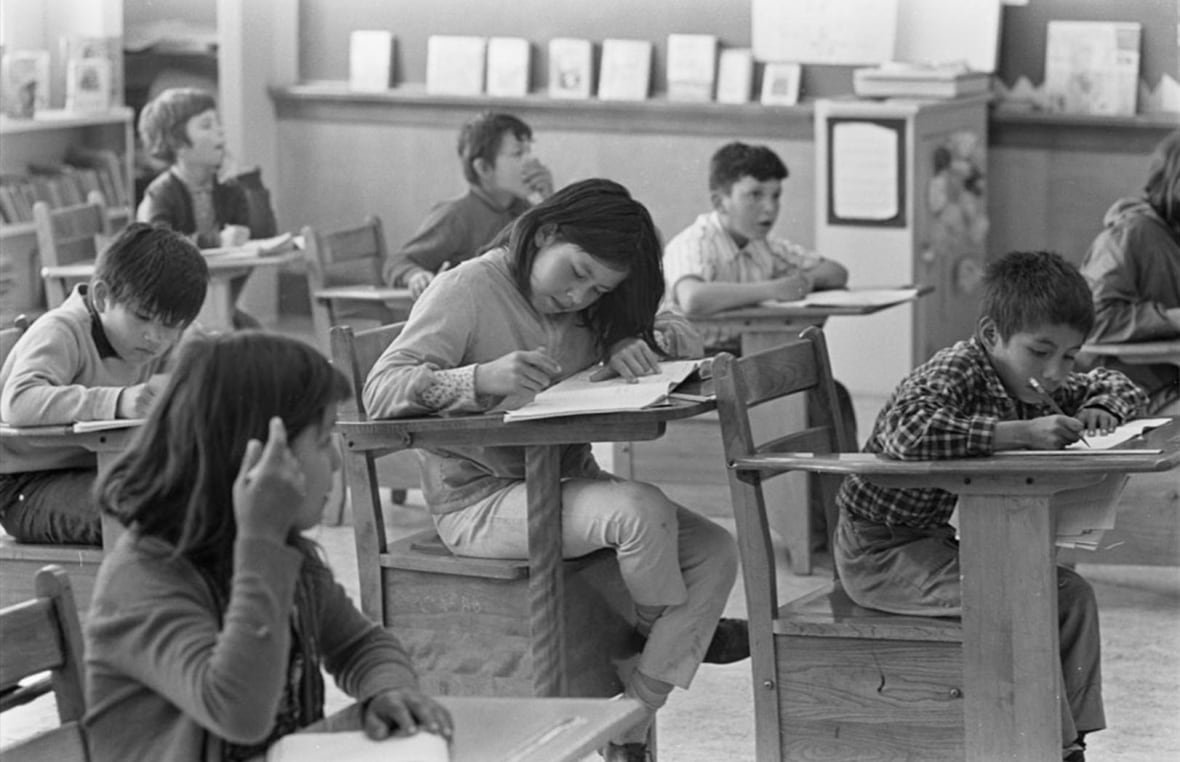 A black-and-white image of students sitting at desks in a classroom.