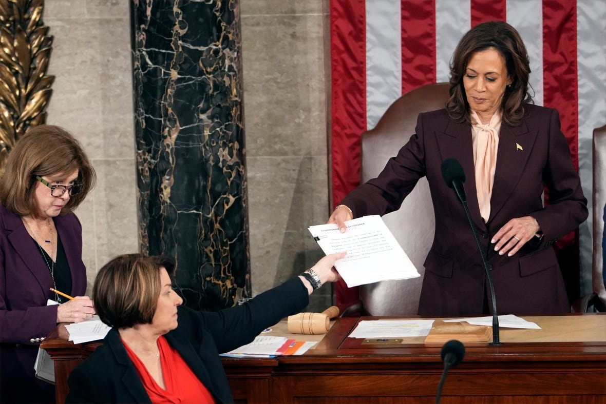 Kamala Harris handing paper across a desk.    