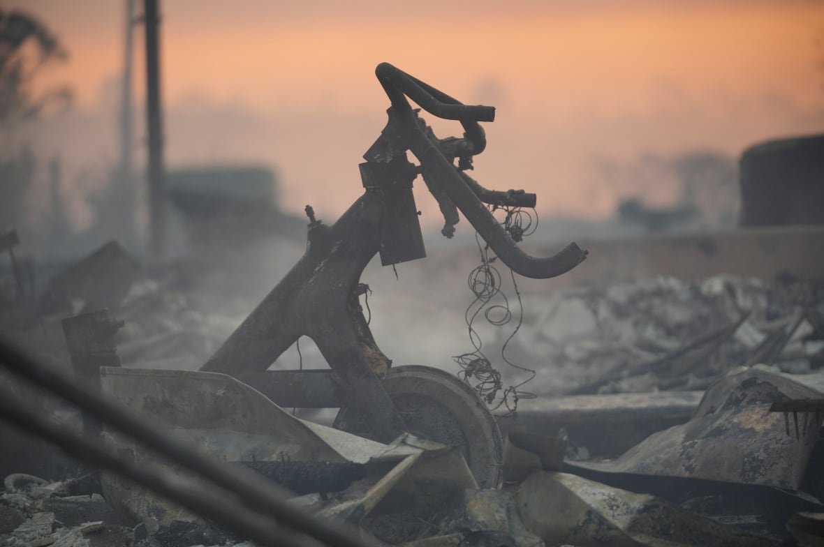 The burnt remains of some sort of metal structure with a wheel attached are visible lying in an assortment of grey rubble. 