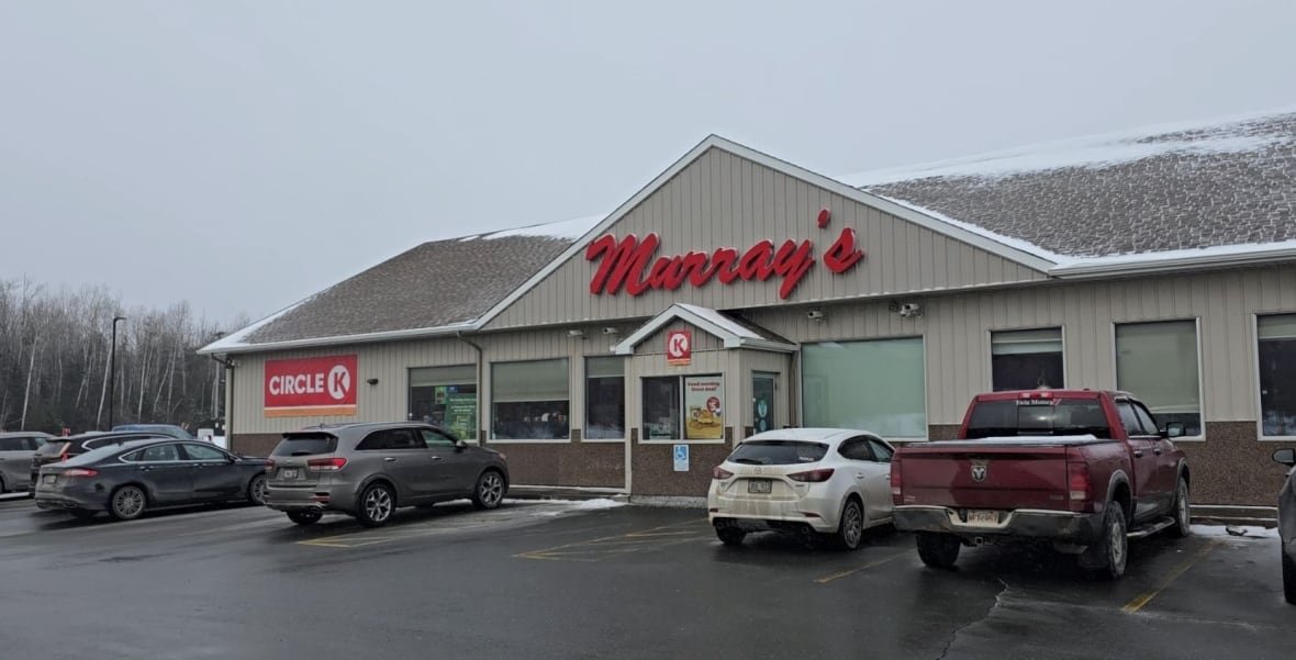 A photo of a tan building with snow on the roof with a sign above the doors in red, handwritten letters that reads "Murray's." Several cars are parked in the front. 