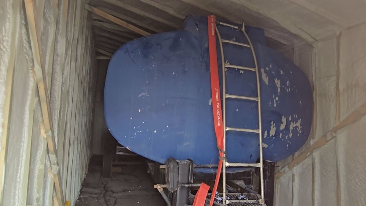 A photo of a large blue water tank on a trailer sitting inside a makeshift building.