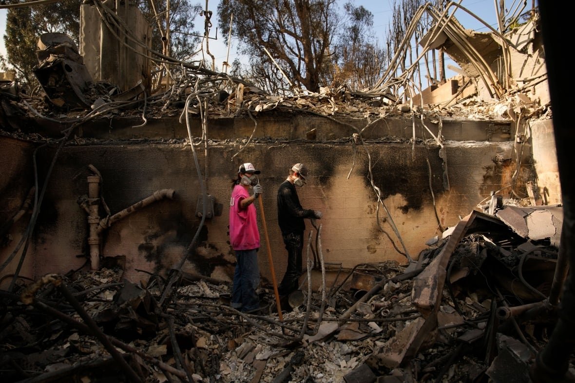 Two people pick through the rubble after a wildfire.