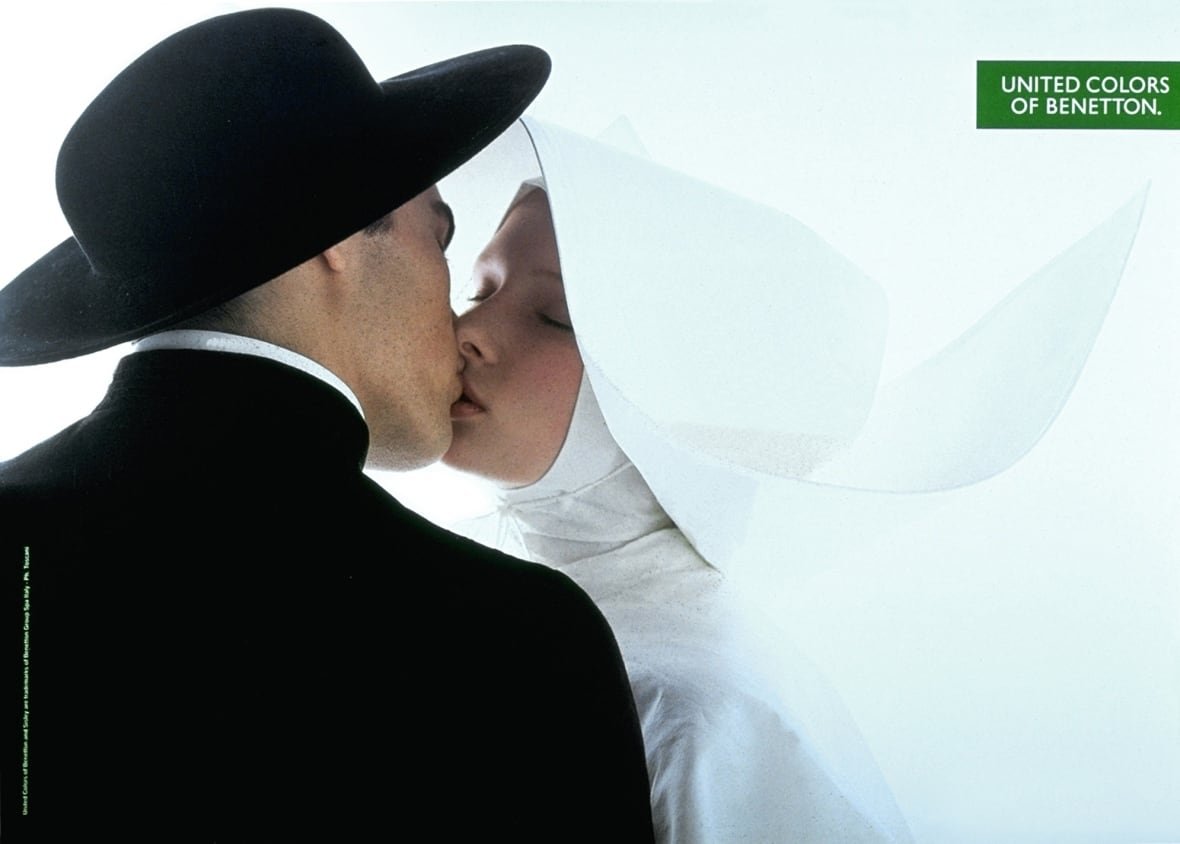 A man in black kisses a woman in all-white. Both appear to be wearing religious garments.