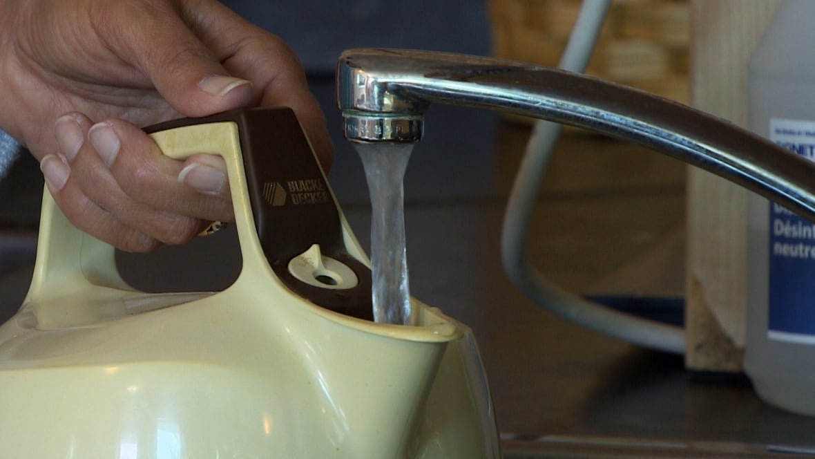 Water from a tap pours into a yellow tea kettle.