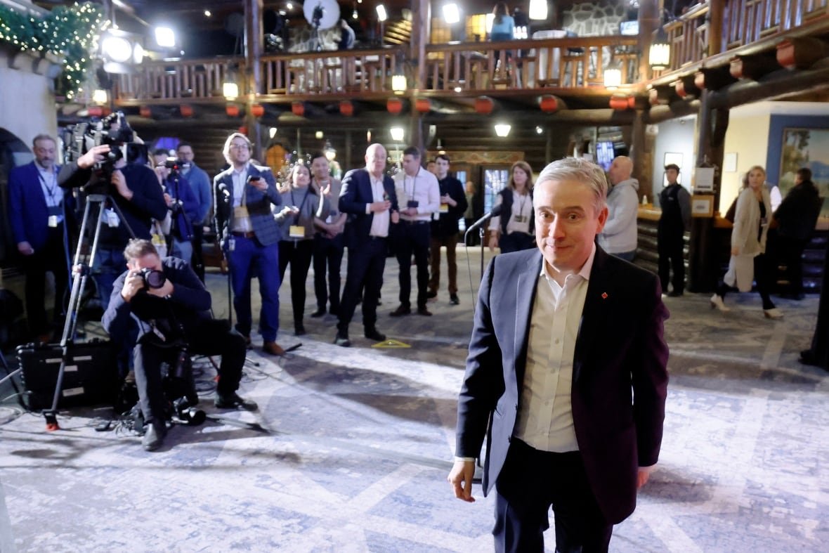 A man walks toward the camera, with a group of reporters behind.