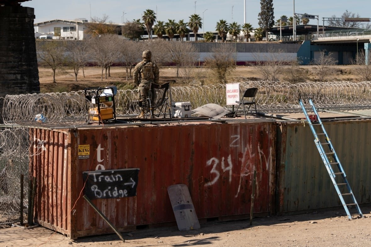 A U.S. National Guardsman stands atop a shipping container and looks across the border towards Mexico from Eagle Pass, Tex.