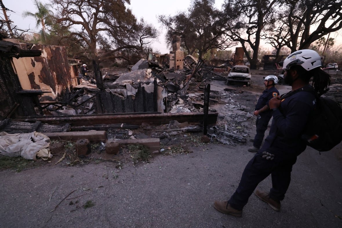 Two people with a search and rescue team look at a home that burned down in a wildfire.