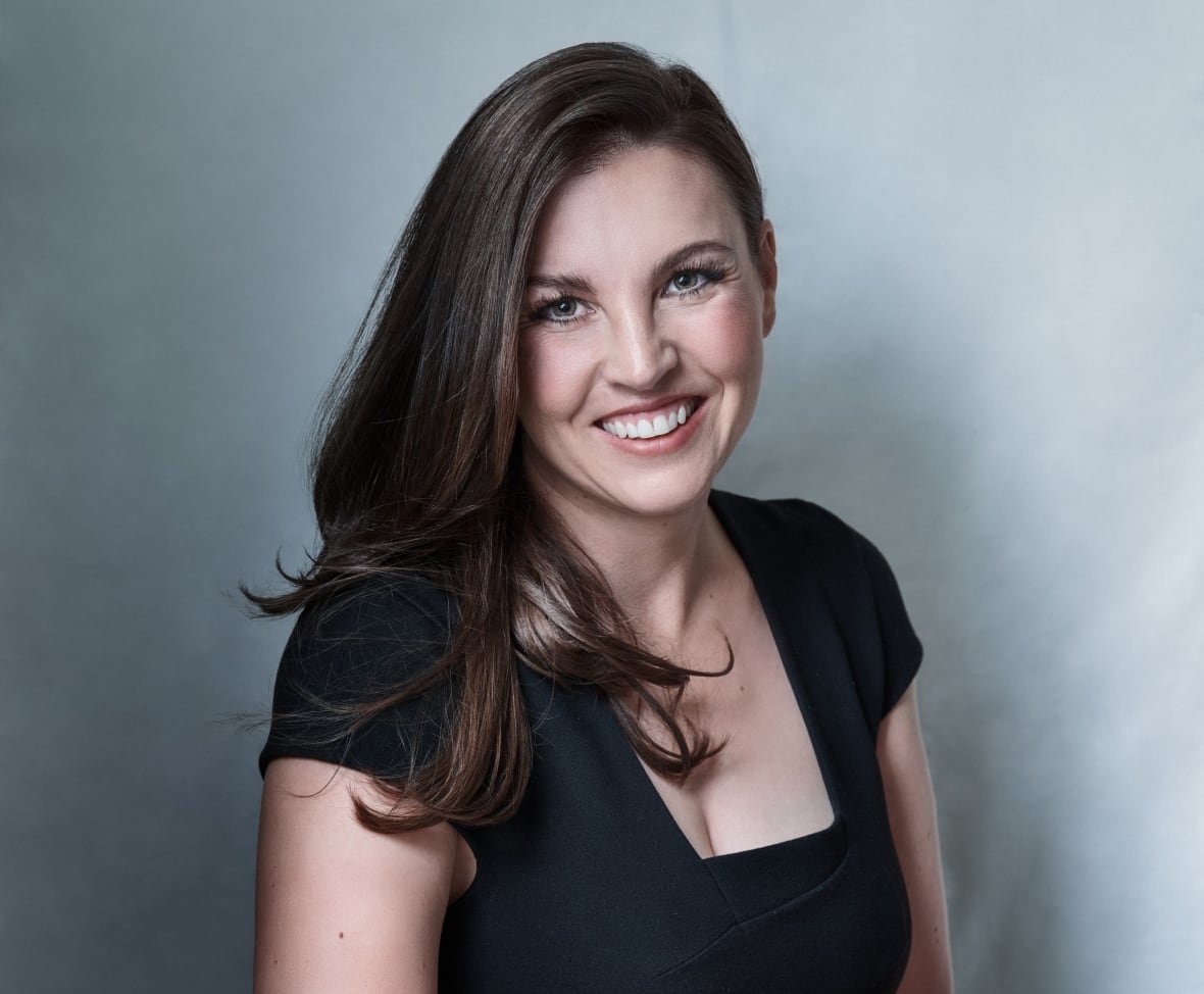 A woman wearing a black dress with long brown hair is smiling at the camera. 