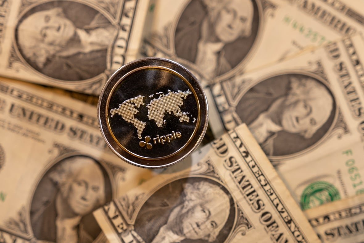 A coin is engraved with the word "Ripple." U.S. bank notes are seen in the background.